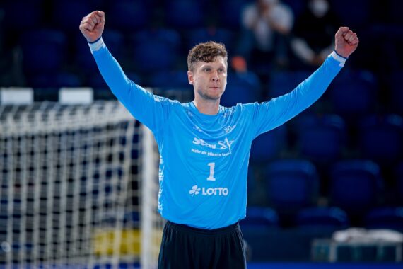 Ein männlicher Handballspieler in einem hellblauen Trikot mit der Nummer 1 steht mit erhobenen Armen jubelnd vor einem Tornetz auf einem Hallenplatz.