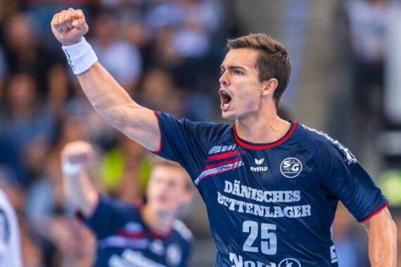 Ein männlicher Handballspieler in einem blauen Trikot mit der Nummer 25 jubelt mit geballter Faust und offenem Mund, als wolle er während eines Spiels jubeln oder schreien. Der Hintergrund ist mit Zuschauern unscharf.