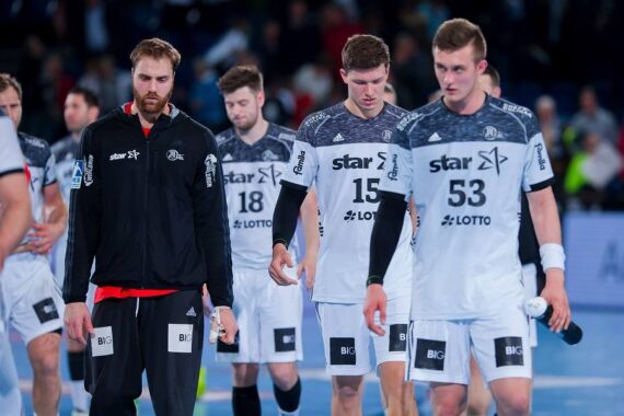 Eine Gruppe männlicher Handballspieler in schwarz-weißen Trikots geht gemeinsam auf das Spielfeld und schaut nach einem Spiel mit ernster oder enttäuschter Miene zu Boden.