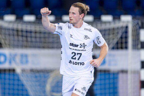 Ein männlicher Handballspieler in einem weißen Trikot mit der Nummer 27 hebt die Faust und scheint vor einem Tor zu feiern. Im Hintergrund ist eine unscharfe Sporthalle zu sehen.