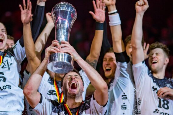 Ein jubelndes Sportteam feiert, während ein Spieler eine große silberne Trophäe hochhält, umgeben von jubelnden Mannschaftskameraden in schwarz-weißen Uniformen.