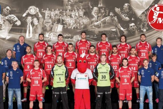Eine Herren-Handballmannschaft in roten Trikots posiert für ein Gruppenfoto mit Trainern und Mitarbeitern. Einige Spieler tragen weiße und grüne Torwarttrikots. Eine Collage vergangener Mannschaftsmomente bildet den Hintergrund, und oben rechts erscheint ein rotes MT-Logo.