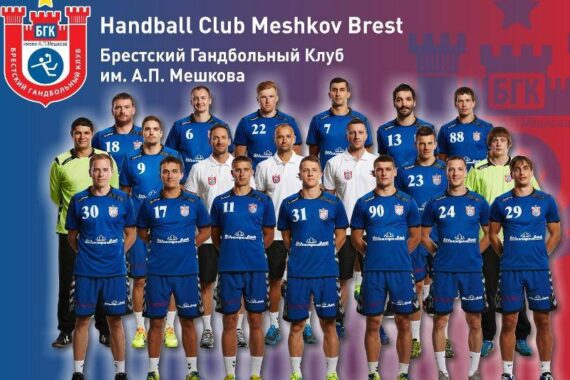 Ein Gruppenfoto der Mannschaft des Handballclubs Meshkov Brest mit 18 männlichen Spielern und Mitarbeitern in blauen Uniformen, die vor einem blauen Hintergrund mit dem Logo und dem Namen des Clubs in Russisch und Englisch stehen und knien.