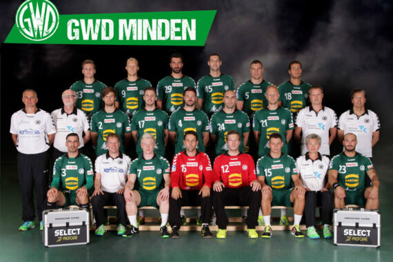 Ein Gruppenfoto der Handballmannschaft und des Personals von GWD Minden, die alle grün-weiße Trikots tragen und in der Halle in drei Reihen mit einem Mannschaftslogo und dem Text "GWD MINDEN" über ihnen posieren.