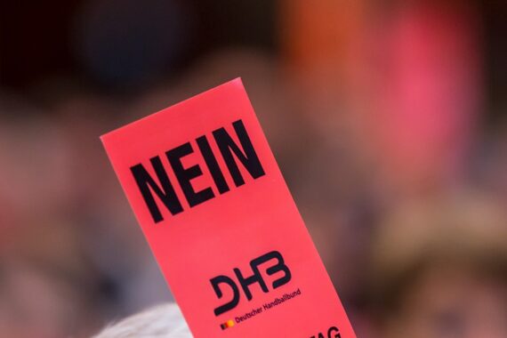 Eine Person hält eine leuchtend rote Karte hoch, auf der in fetten schwarzen Buchstaben das Wort NEIN und darunter das Logo des DHB (Deutscher Handballbund) steht.