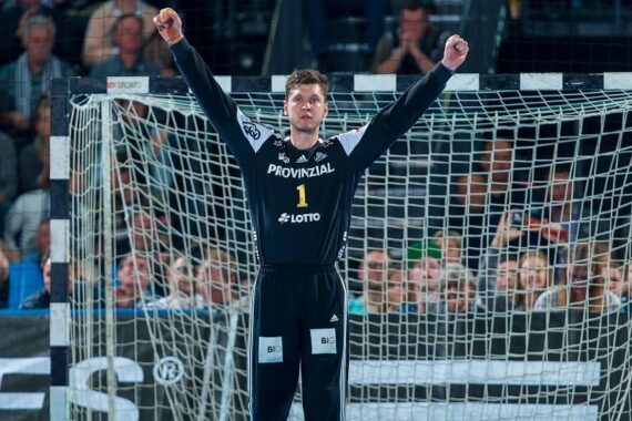 Ein Handballtorwart in einem schwarzen Trikot mit der Nummer 1 steht mit erhobenen Armen jubelnd vor dem Tor. Im Hintergrund ist eine Menge von Zuschauern zu sehen.