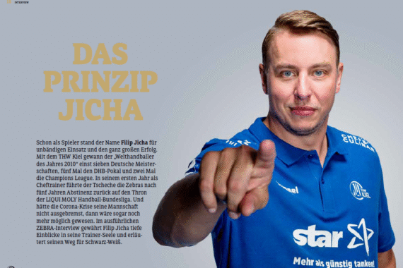 Ein Mann in einem blauen Polohemd mit Sponsorenlogos steht vor einem schlichten hellen Hintergrund und zeigt in die Kamera. Auf der linken Seite des Bildes ist der deutsche Text "Das Prinzip Jicha" zu lesen.