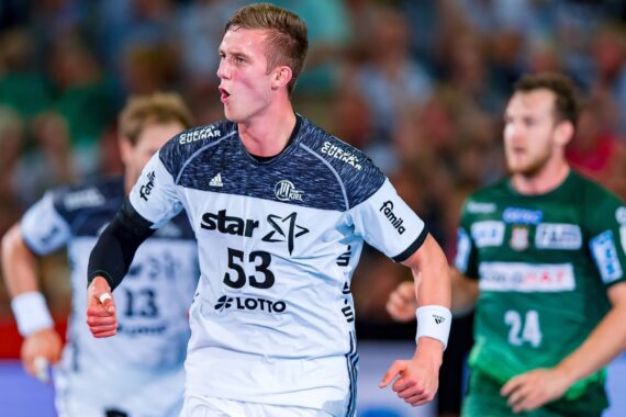 Ein männlicher Handballspieler in einem weiß-schwarzen Trikot mit der Nummer 53 läuft über das Spielfeld und scheint zu schreien, während im Hintergrund ein anderer Spieler in einem grünen Trikot zu sehen ist.