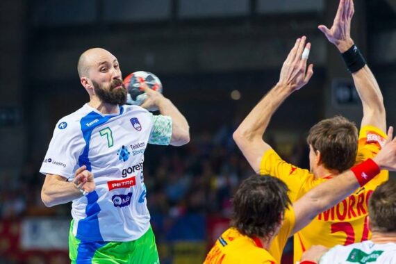 Ein Handballspieler in einem weiß-grünen Trikot springt und bereitet sich auf den Wurf vor, während drei Verteidiger in gelben Trikots versuchen, ihn während eines Spiels zu blockieren.