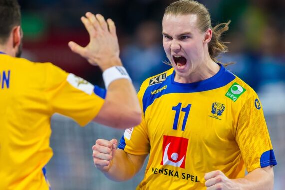 Ein männlicher Handballspieler in einem gelben Trikot mit der Nummer 11 schreit während eines Spiels leidenschaftlich und hebt die Faust. Ein anderer Spieler, ebenfalls in Gelb, steht ihm mit erhobener Hand gegenüber, als würde er feiern.
