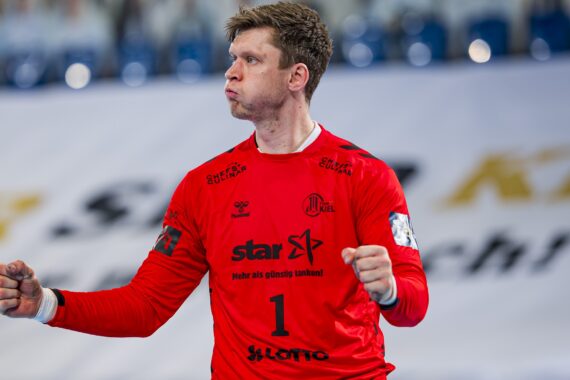 Ein männlicher Handballtorwart, der ein rotes Trikot mit der Nummer 1 trägt, ballt beide Fäuste und blickt entschlossen zur Seite, während eines Spiels.