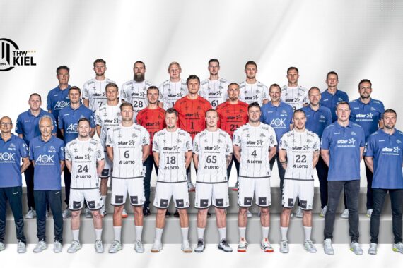 Eine Handballmannschaft stellt sich für ein offizielles Gruppenfoto auf. Die Spieler in weißen Trikots und die Trainer in blauen Hemden stehen in einer Reihe vor einem weißen Hintergrund, auf dem das Logo des THW Kiel zu sehen ist.