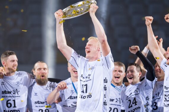 Eine Gruppe jubelnder männlicher Athleten in weißen Trikots feiert, während ein Spieler eine glänzende silberne Trophäenplatte über seinen Kopf hebt und goldenes Konfetti um sie herum fällt.