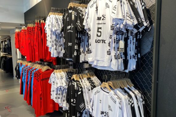 In einem modernen Einzelhandelsgeschäft hängen reihenweise rote, schwarze und weiße Sporttrikots mit verschiedenen Nummern und Logos in den Regalen.