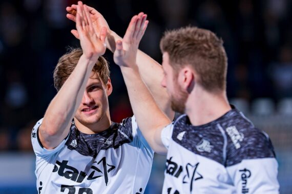 Zwei männliche Athleten in weißen und schwarzen Sporttrikots geben sich beim Feiern während eines Spiels ein High Five. Die Szene ist hell beleuchtet und hat einen unscharfen Hintergrund.