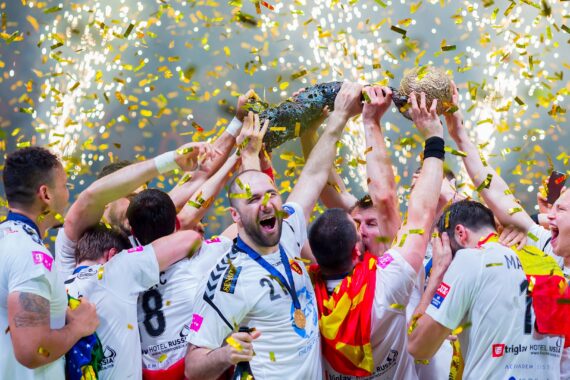 Ein jubelndes Sportteam in weißen Trikots feiert und hebt gemeinsam einen Pokal inmitten eines goldenen Konfettiregens. Die Spieler lächeln und jubeln, die Medaillen hängen ihnen um den Hals.