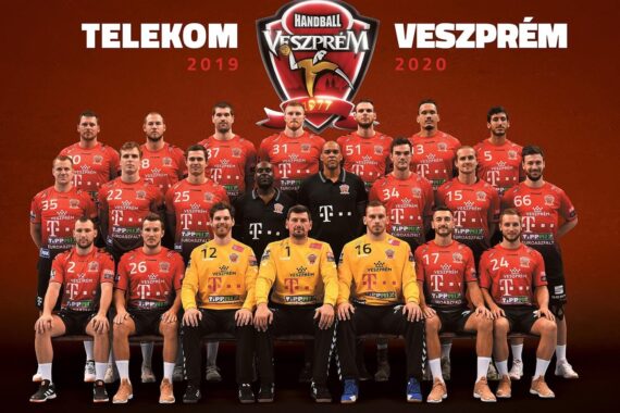 Ein Gruppenfoto der Handballmannschaft 2019-2020 von Telekom Veszprém mit Spielern und Mitarbeitern in roten Trikots und zwei in gelben Trikots, die gemeinsam vor einem Teamlogo und einem Text posieren.