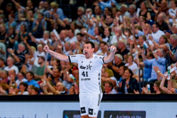 Ein Handballspieler in einem weißen Trikot mit der Nummer 41 jubelt mit erhobenen Armen vor einer jubelnden Menge in einer Sporthalle.