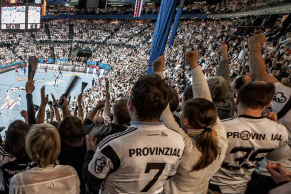 Eine große Menge begeisterter Fans, zumeist in weiß gekleidet und in Provinzial-Trikots, jubelt und reckt während eines Handballspiels in einem Hallenstadion die Arme in die Höhe.