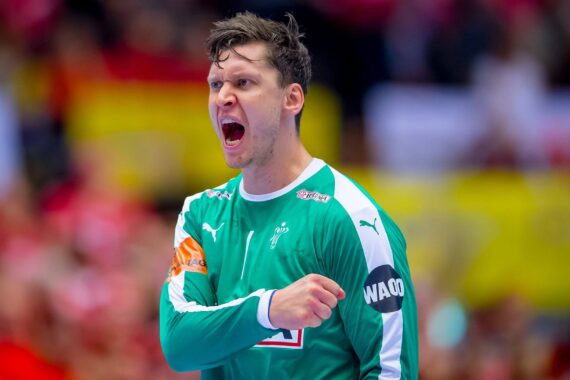 Ein männlicher Handballspieler in einem grünen Trikot schreit leidenschaftlich und ballt während eines Spiels die Faust zum Jubel. Der Hintergrund zeigt eine unscharfe Menschenmenge in einem Stadion.