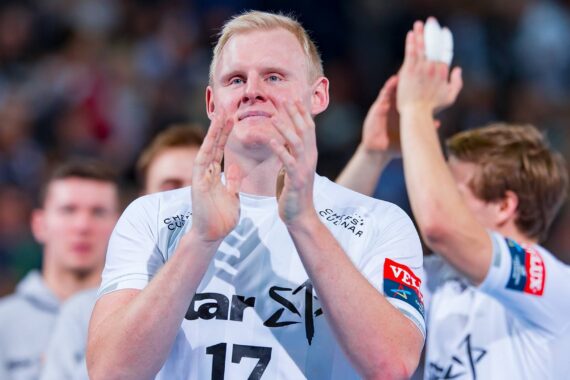 Ein männlicher Sportler in einem weißen Trikot mit der Nummer 17 klatscht, während andere Mannschaftskameraden im Hintergrund klatschen. Die Szene scheint eine Sportveranstaltung mit einer unscharfen Menschenmenge zu sein.