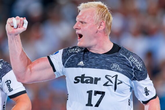 Ein männlicher Handballspieler in einem weiß-schwarzen Trikot mit der Nummer 17 ballt während eines Spiels die Faust und jubelt, während die Zuschauer im Hintergrund verschwommen zu sehen sind.