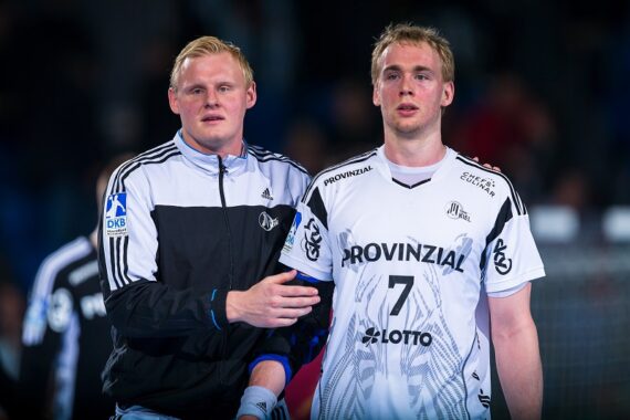 Zwei männliche Sportler in Sportkleidung stehen nebeneinander; der eine trägt eine schwarz-weiße Jacke und hält sanft den Arm des anderen, der ein weißes Trikot mit der Nummer 7 und der Aufschrift Provinzial trägt.