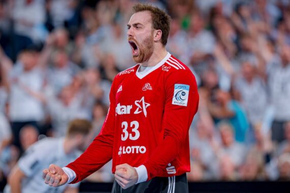 Ein Handballspieler im roten Trikot mit der Nummer 33 feiert leidenschaftlich mit geballten Fäusten und weit aufgerissenem Mund, umgeben von einer verschwommenen Menschenmenge im Hintergrund.