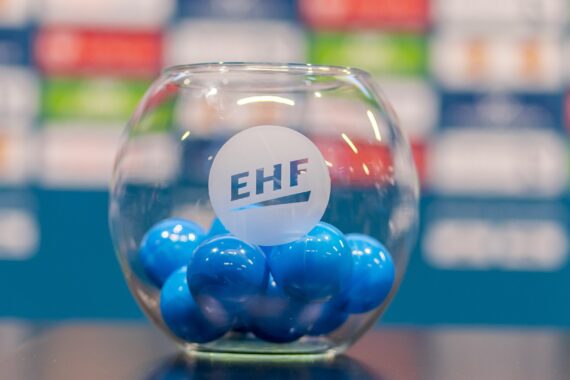 Eine transparente Glasschale mit dem EHF-Logo ist mit blauen Kugeln gefüllt. Die Schale steht auf einem Tisch mit einem unscharfen Hintergrund, der bunte, unscharfe Rechtecke zeigt.