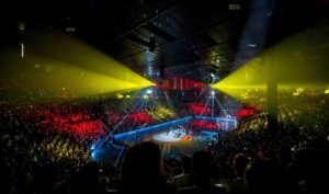 Eine überfüllte Sporthalle mit bunten Lichtern, die auf die Zuschauer und das Basketballfeld scheinen und eine dramatische und festliche Atmosphäre während einer Veranstaltung schaffen.