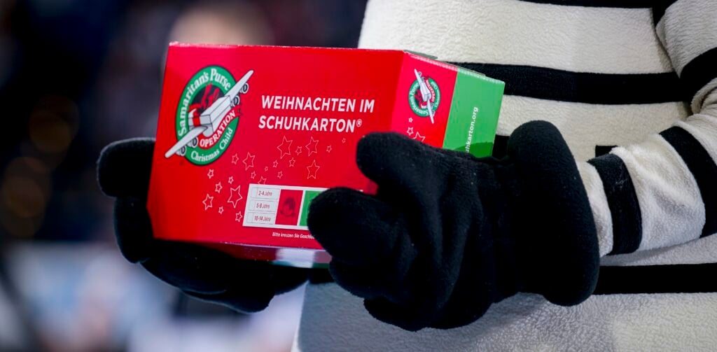 Handball, Bundesliga 2022/23: THW Kiel - TBV Lemgo Lippe Eine Person in schwarz-weiß gestreifter Kleidung, die an einen THW Kiel Handball-Fan erinnert, hält einen rot-grünen Schuhkarton mit der Aufschrift