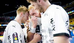 Drei männliche Handballer im weißen Trikot umarmen sich emotional auf dem Spielfeld, einer scheint sich das Gesicht zu wischen oder zu weinen - ein intensiver Moment des DHB-Pokalsiegs des THW Kiel Saison 2024/2025.