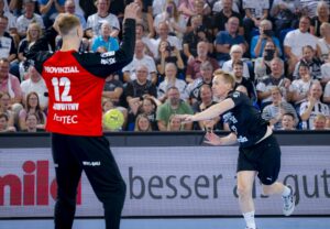 Ein Handballer in Schwarz vom THW Kiel schießt den Ball in Richtung Tor, während der Torhüter in Rot sich zur Wehr setzt. Die Zuschauer in der Ostseehalle verfolgen diesen intensiven Moment der THW Kiel Saison 2025, der den emotionalen Abschied von Patrick Wiencek markiert.