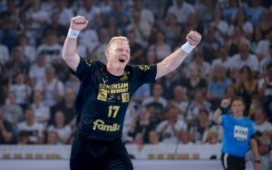 Ein Handballer im dunkelblauen THW Kiel-Trikot mit der Nummer 17 feiert mit erhobenen Armen auf dem Spielfeld, während die Zuschauer in der Ostseehalle Patrick Wienceks Abschied in der Saison 2025 bejubeln.