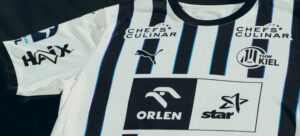 Ein weißes Sporttrikot mit vertikalen schwarzen Streifen, auf denen die Logos von Puma, Chefs Culinar, Haix, ORLEN, star und das Abzeichen des Handballvereins THW Kiel abgebildet sind.