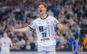 THW Kiel Kapitän Rune Dahmke, der die weiße Trikotnummer 23 trägt, feiert leidenschaftlich mit geballten Fäusten und offenem Mund während eines Spiels der Handball-Bundesliga. Im Hintergrund sind unscharfe Zuschauer und andere Spieler auf dem Spielfeld zu sehen.