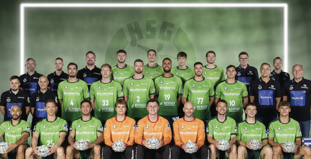 25_vor_HSG_Team Eine Herren-Handballmannschaft posiert für ein Gruppenfoto in grün-schwarzen Trikots, hält Handbälle in der Hand und die Trainer stehen dahinter. Der Hintergrund zeigt einen grünen Farbverlauf und ein großes HSG-Logo.