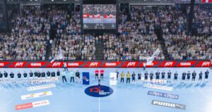 Eine Handballmannschaft stellt sich auf einem blauen Hallenplatz vor einer vollbesetzten Arena mit jubelnden Fans auf, in der Mitte des Platzes stehen Schiedsrichter und Offizielle. Maskottchen halten Fahnen, und im Hintergrund sind eine Anzeigetafel und Werbung zu sehen.