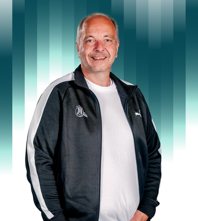 THWKiel-Christian_Robohm Ein lächelnder Mann mittleren Alters mit kurzen grauen Haaren und einem Bart trägt eine schwarz-weiße Puma-Trainingsjacke über einem weißen Hemd und steht vor einem geometrischen Hintergrund mit blaugrünem und weißem Farbverlauf.