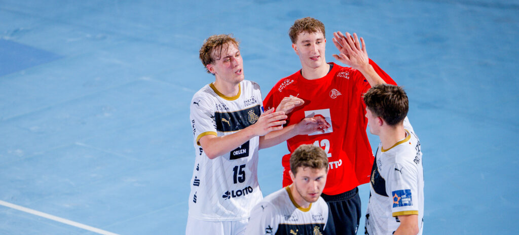251021_THW_Ostrovia_Titel_Youngster Drei männliche Sportler auf einem Hallenplatz, zwei in weißen Trikots und einer in einem roten Trikot, tauschen High-Fives und Gesten aus, mit einem weiteren Spieler in Weiß im Vordergrund. Die Szene deutet auf eine Interaktion nach dem Spiel hin.