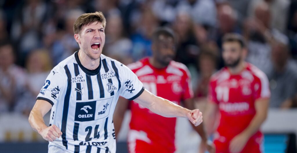 HANDBALL 2025/26: THW Kiel - MT Melsungen Ein männlicher Handballspieler in einem schwarz-weiß gestreiften Trikot jubelt leidenschaftlich auf dem Spielfeld und ballt die Fäuste, während im Hintergrund zwei Gegner in roten Trikots stehen.