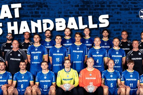 Eine Handballmannschaft stellt sich in drei Reihen vor einer dunklen Backsteinwand auf. Die meisten Spieler tragen blaue Trikots, einige wenige sind schwarz und zwei orange. Oben auf den Trikots stehen "Heimat des Handballs" und Logos.
