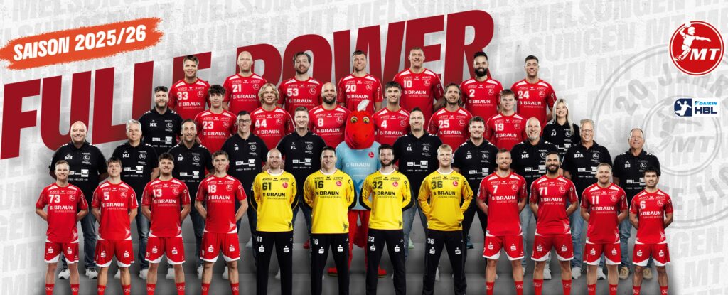 Eine Profi-Handballmannschaft posiert für ein Gruppenfoto in drei Reihen mit rot-schwarzen Trikots, über denen 
