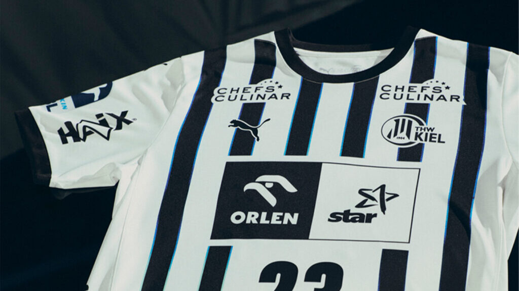 Ein schwarz-weiß gestreiftes Handballtrikot des THW Kiel mit Sponsorenlogos von Puma, Chefs Culinar, HAX, Orlen und Star. Die Nummer 23 ist teilweise am unteren Rand sichtbar.