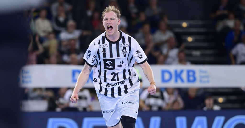 HANDBALL 2025/26: THW Kiel - Rhein-Neckar Löwen Ein männlicher Handballspieler in einem schwarz-weiß gestreiften Trikot mit der Nummer 21 jubelt leidenschaftlich auf dem Spielfeld, mit offenem Mund und geballten Fäusten. Im unscharfen Hintergrund sind Zuschauer zu sehen.