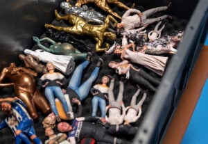 Eine Aufbewahrungsbox, gefüllt mit kleinen, detaillierten Figuren von Menschen und Tieren in verschiedenen Posen, einige in realistischen Farben bemalt und andere in metallischem Gold oder Silber, alle auf einer schwarzen Schaumstoffeinlage angeordnet.