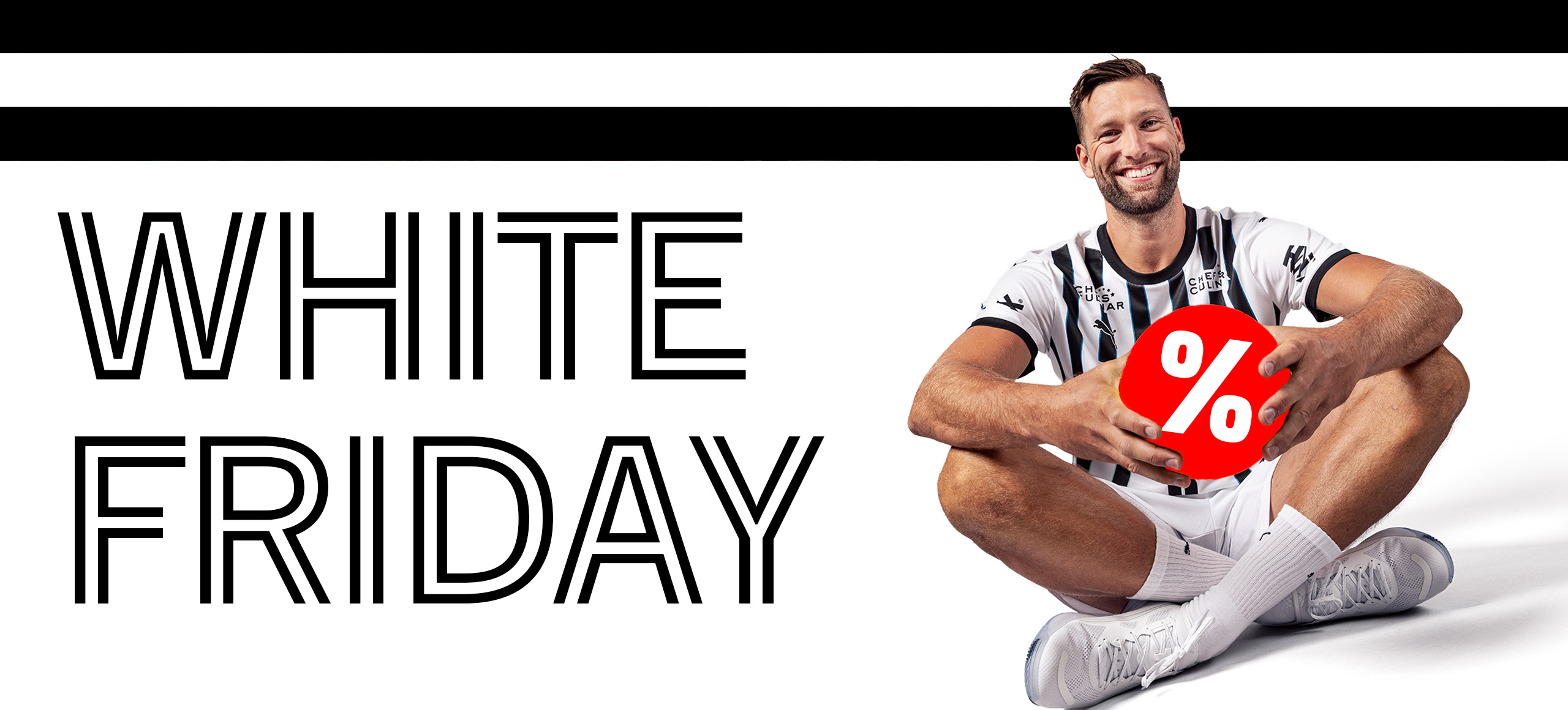 Ein Mann in einem schwarz-weißen Sportdress sitzt lächelnd da und hält einen roten Ball mit einem weißen Prozentzeichen. Neben ihm steht in großer Schrift WHITE FRIDAY auf weißem Hintergrund mit schwarzen Streifen.