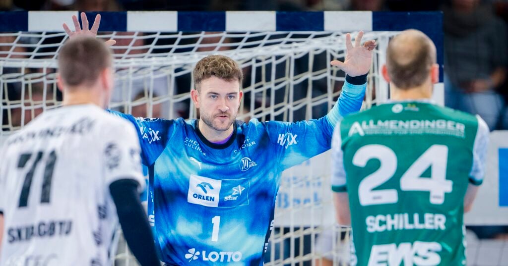 HANDBALL 2025/26: THW Kiel - Frisch Auf! Göppingen Ein Handballtorwart in einem blauen Trikot steht während eines Spiels mit erhobenen Armen aufmerksam vor zwei gegnerischen Spielern in weißen und grünen Trikots in der Nähe des Tornetzes.