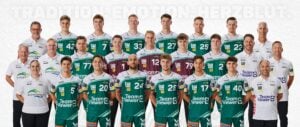 Eine Herren-Volleyballmannschaft und ihre Betreuer posieren für ein offizielles Gruppenfoto. Alle tragen grüne, weiße oder kastanienbraune Trikots mit Sponsorenlogos und stehen oder knien in Reihen vor einem weißen Hintergrund.