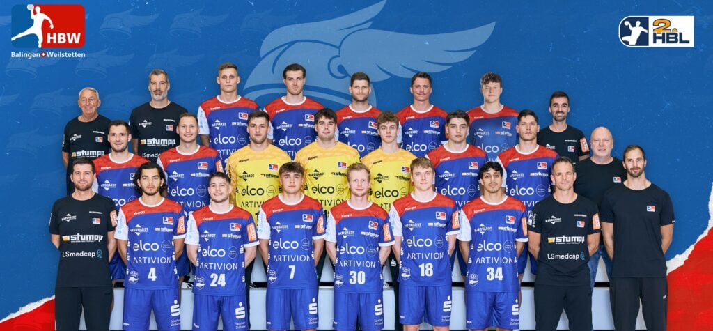 Eine Handballmannschaft der Männer posiert für ein Gruppenfoto in roten und blauen Trikots mit Sponsorenlogos, stehend und sitzend in Reihen vor einem blauen Hintergrund mit Team- und Ligalogos. Trainer und Betreuer sind in Schwarz gekleidet.